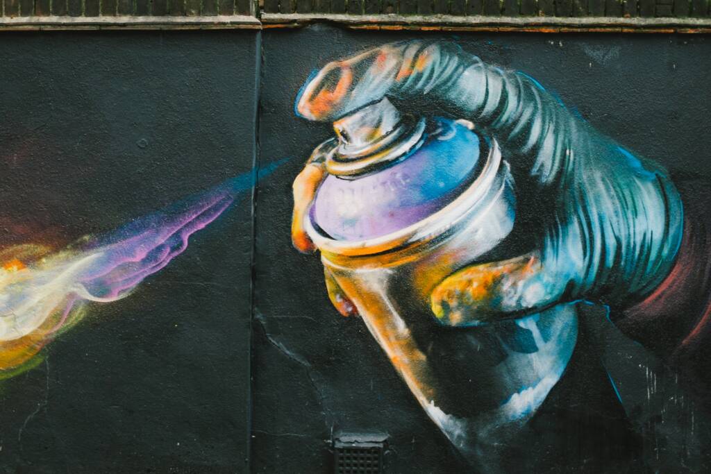 Graffiti na ścianie przedstawiające rękę używającą sprayu z farbą. Preparat Sagraf zapobiega tworzeniu graffiti.